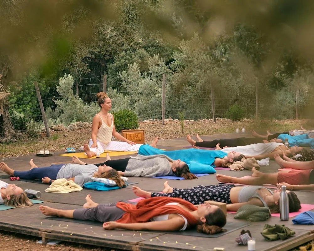 Group of travelers practicing yoga outdoors surrounded by olive trees in Oludeniz, Turkey.