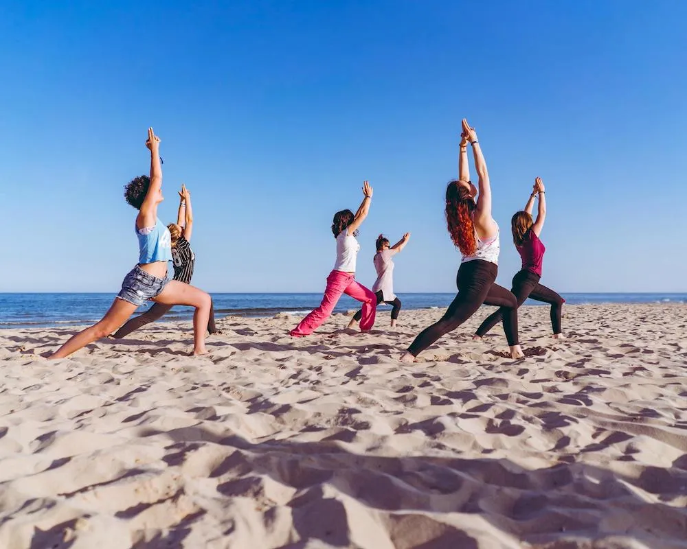 Travelers practicing energizing morning yoga on the sandy beach by the sea.