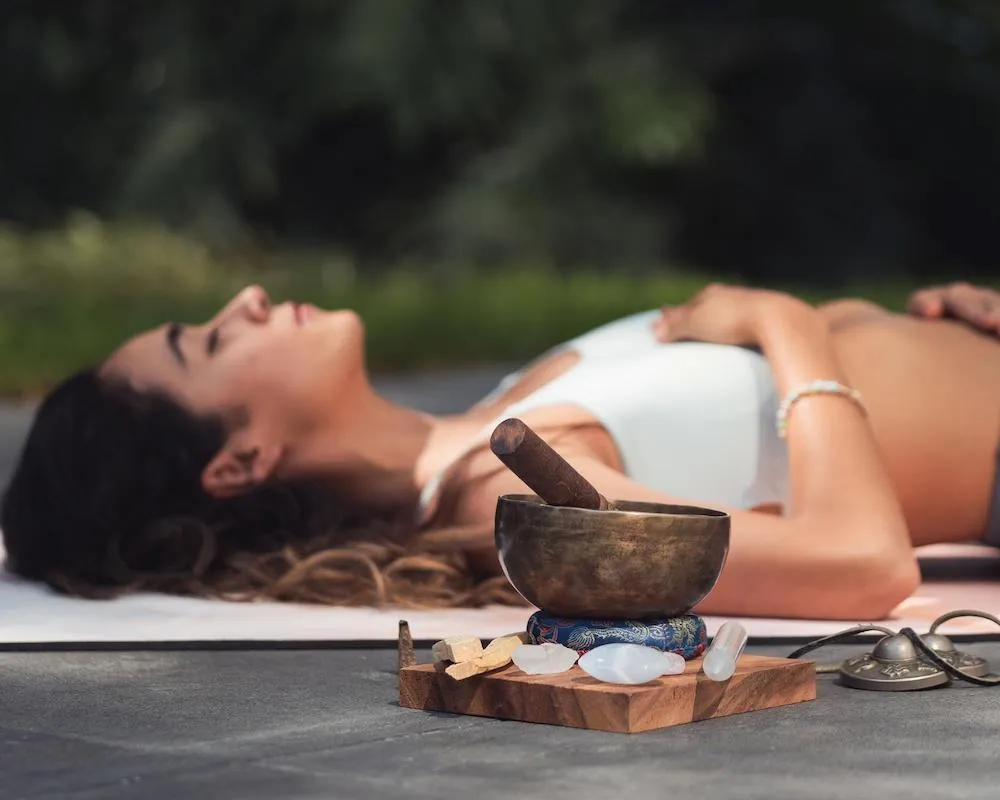 Woman practicing sound healing and deep relaxation outdoors during a yoga retreat.