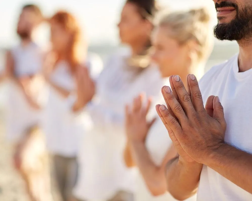Group of travelers practicing mindfulness and connection through prayer gestures during a wellness retreat.