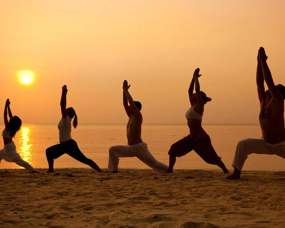Group practicing yoga poses on the beach at sunset in Oludeniz, Turkey.