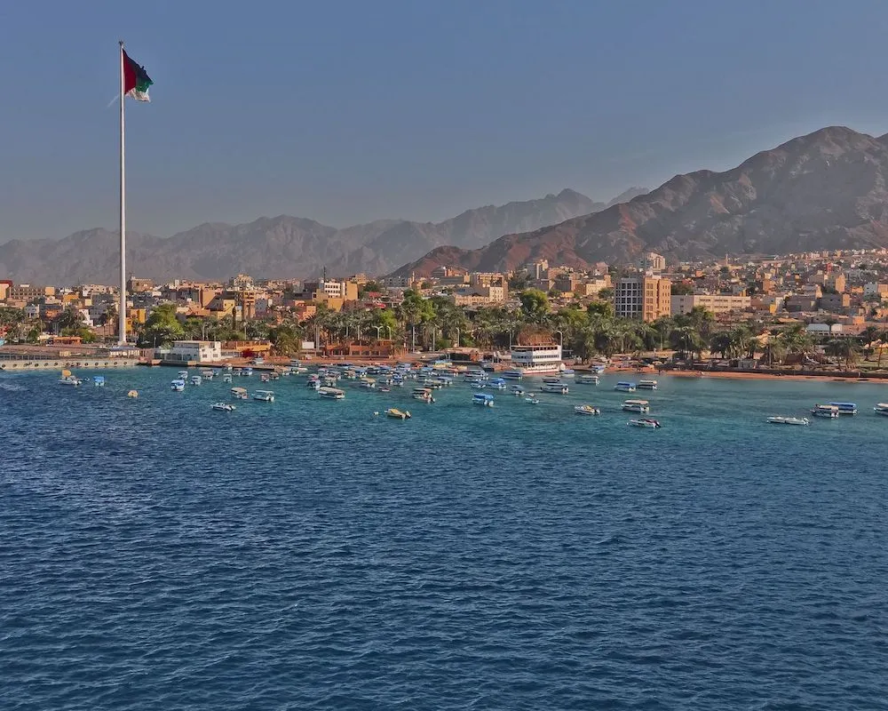 Panoramic view of Aqaba’s coastline with boats and cityscape against desert mountains.